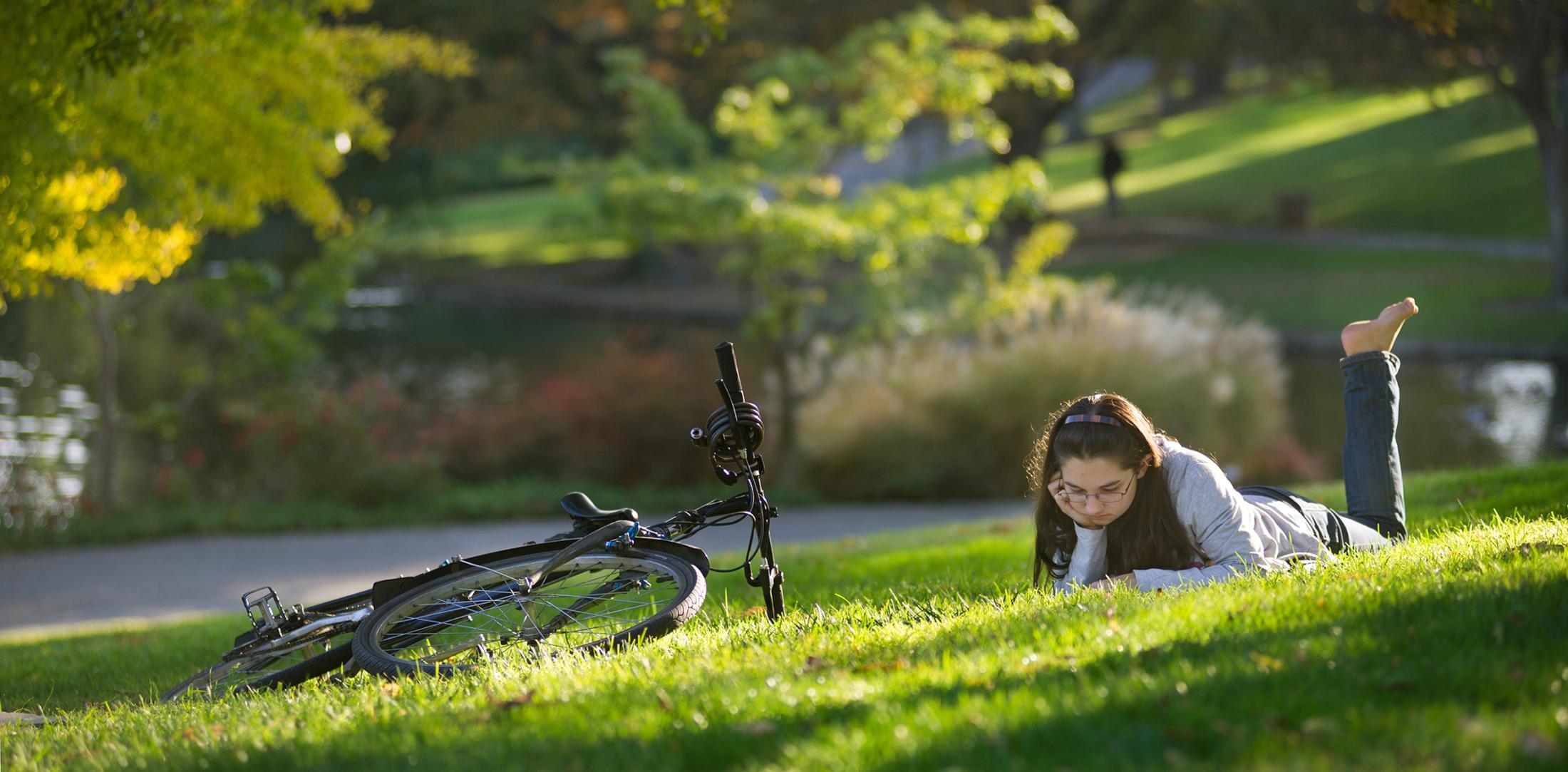 female student studies on the grass near Lake Spafford in the Arborteum